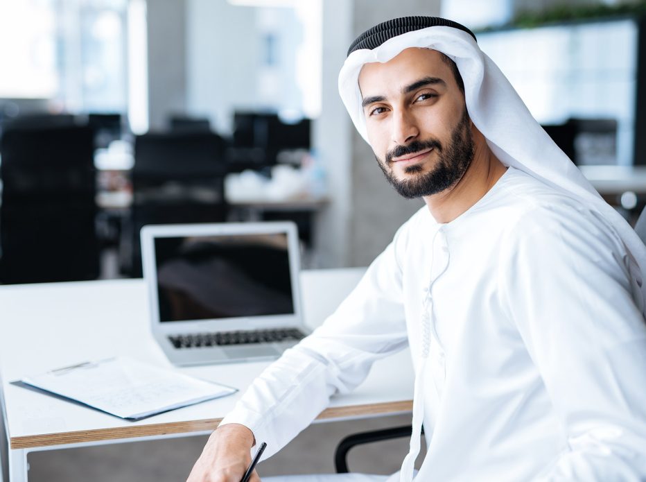 Handsome man with dish dasha working in his business office of Dubai. Portraits of a successful businessman in traditional emirates white dress. Concept about middle eastern cultures, lifestyle and professional occupations
